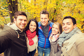 technology, season, friendship and people concept - group of smiling men and women taking selfie with smartphone or camera in autumn park