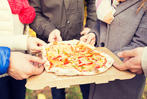friendship, junk food and people concept - close up of friends hands eating pizza from cardboard box outdoors