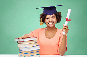 education, school, knowledge, graduation and people concept - happy smiling african american student girl in bachelor cap with books and diploma over green chalk board background