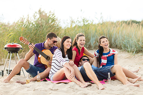 summer holidays, vacation, music, happy people concept - group of happy friends having picnic and playing guitar on beach