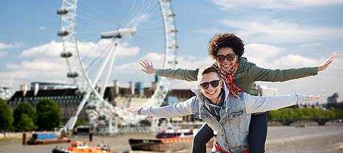 friendship, leisure, international, freedom and people concept - happy teenage couple in shades having fun over london ferry wheel background