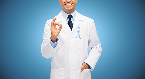 healthcare, profession, people, gesture and medicine concept - close up of smiling male doctor in white coat with sky blue prostate cancer awareness ribbon showing ok hand sign