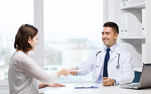 medicine, health care, meeting and people concept - smiling doctor with clipboard and laptop computer giving medical prescription or certificate to young woman at hospital