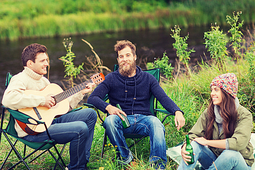 adventure, travel, tourism and people concept - group of smiling tourists playing guitar and drinking beer in camping