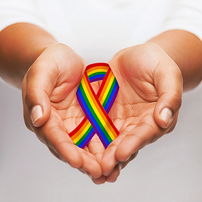 homosexuality, support and charity concept - african american woman hands holding rainbow gay pride awareness ribbon
