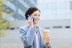 business and people concept - young smiling woman calling on smartphone and drinking coffee over office building in city