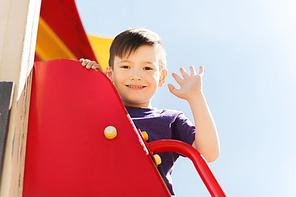 summer, childhood, leisure, gesture and people concept - happy little boy waving hand on children playground climbing frame
