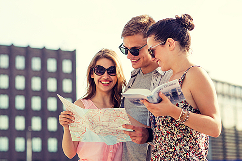 friendship, travel, tourism, vacation and people concept - smiling friends with map and city guide outdoors