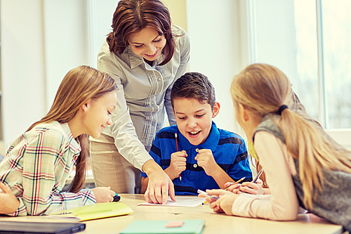 education, elementary school, learning and people concept - teacher helping school kids writing test in classroom