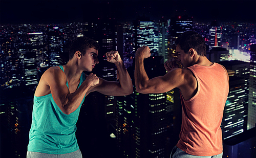 sport, competition, strength and people concept - young men fighting hand-to-hand over night city background