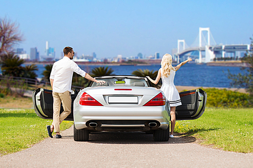 people, travel, tourism and road trip concept - happy man and woman near cabriolet car over river and tokyo  bridge background