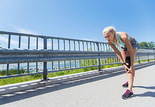 fitness, sport, exercising and healthy lifestyle concept - young woman with knee support brace injured leg outdoors