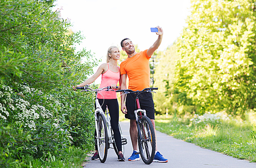 fitness, sport, people, technology and healthy lifestyle concept - happy couple with bicycle taking selfie by smartphone outdoors