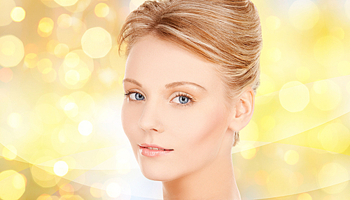 beauty, people, holidays and health concept - beautiful young woman face over yellow lights background