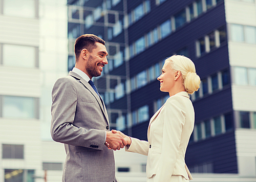 business, partnership, gesture success and people concept - smiling businessman and businesswoman shaking hands over office building