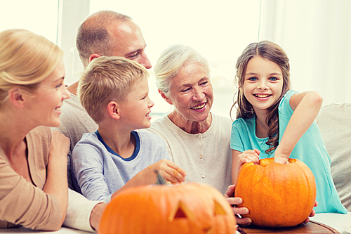 family, happiness, generation, holidays and people concept - happy family making halloween pumpkins at home