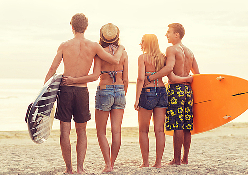 friendship, sea, summer vacation, water sport and people concept - group of smiling friends wearing swimwear with surfboards on beach from back