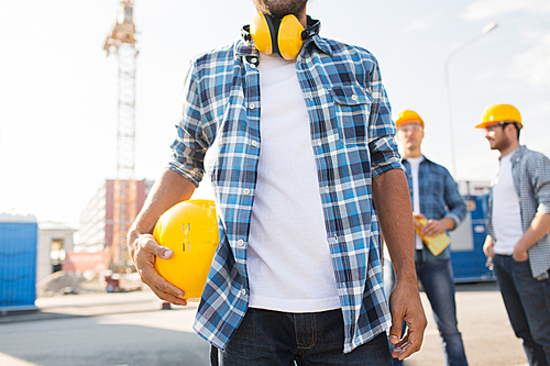 building, construction, protective gear and people concept - close up of builder holding yellow hardhat or helmet outdoors