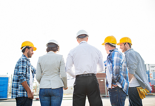 business, building, teamwork and people concept - group of builders and architects in hardhats with blueprint on construction site