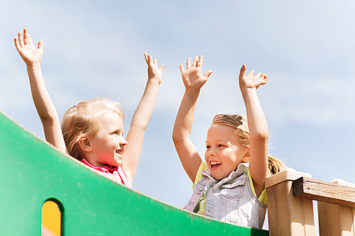 summer, childhood, leisure, friendship and people concept - happy little girls waving hands on children playground climbing frame