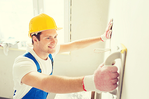 business, building, profession and people concept - smiling builder with grinding tool indoors