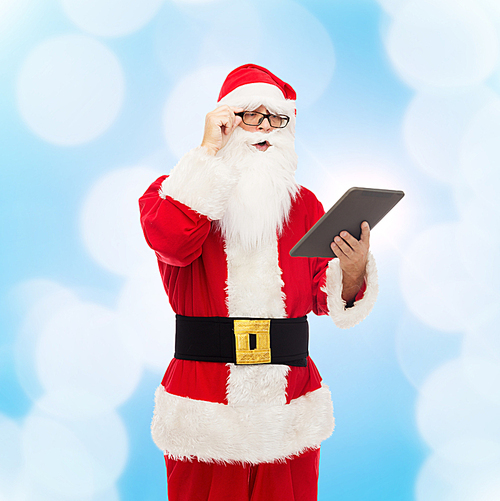 christmas, holidays, technology and people concept - man in costume of santa claus with tablet pc computer over blue lights background