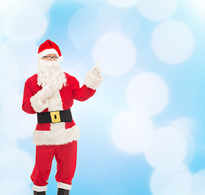 christmas, holidays, gesture and people concept - man in costume of santa claus pointing fingers over blue lights background
