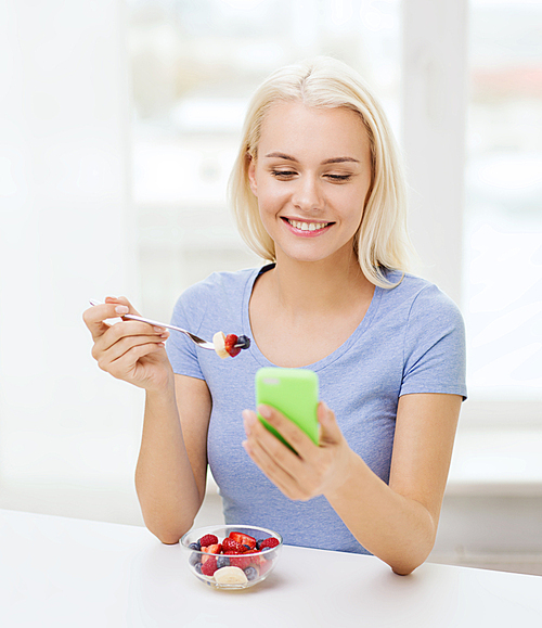 healthy eating, ing and people concept - smiling young woman with smartphone eating fruit salad at home