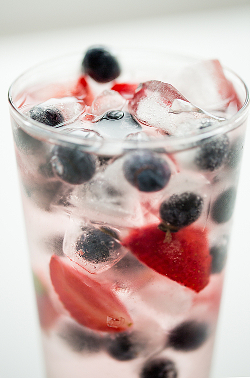 healthy eating, drinks,  and detox concept - close up of fruit water with strawberry, blackcurrant or blueberry and ice cubes in glass