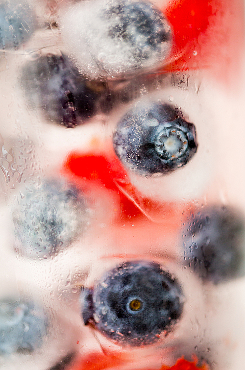 healthy eating, drinks, diet and detox concept - close up of fruit water with strawberry, blackcurrant or blueberry and ice cubes over glass