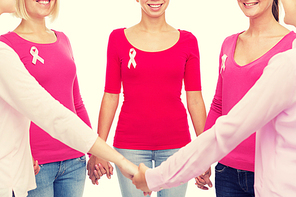 healthcare, people and medicine concept - close up of smiling women in blank shirts with pink breast cancer awareness ribbons holding hands over white background