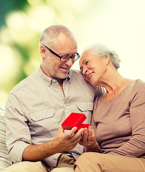 family, holidays, age and people concept - happy senior couple with little red gift box over green background