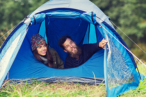 camping, travel, tourism, hike and people concept - smiling couple of tourists looking out from tent