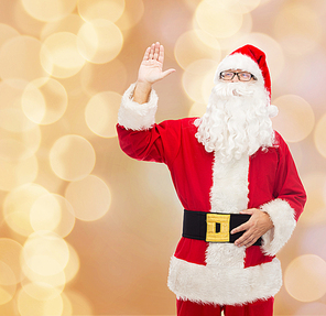 christmas, holidays, gesture and people concept - man in costume of santa claus waving hand over beige lights background