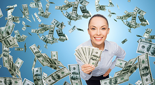 business, money, finance, people and banking concept - smiling businesswoman with heap of dollar cash money over blue background
