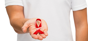 medicine, health care, charity and people concept - close up of male hand holding red hiv aids or heart disease awareness ribbon