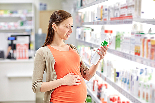 pregnancy, medicine, pharmaceutics, health care and people concept - happy pregnant woman choosing anti stretch marks lotion at pharmacy