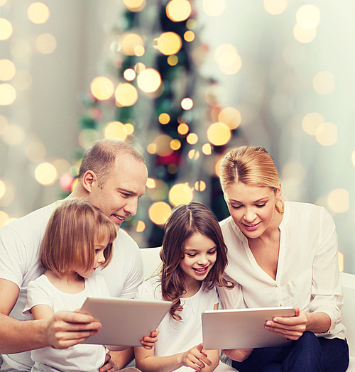 family, holidays, technology and people - smiling mother, father and little girls with tablet pc computers over christmas tree lights background