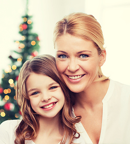 family, childhood, holidays and people - smiling mother and little girl over christmas tree background