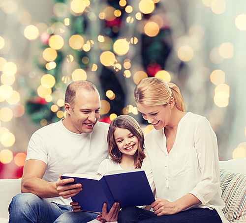 family, childhood, holidays and people - smiling mother, father and little girl reading book over living room and christmas tree background