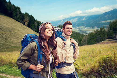 adventure, travel, tourism, hike and people concept - smiling couple walking with backpacks over alpine hills background