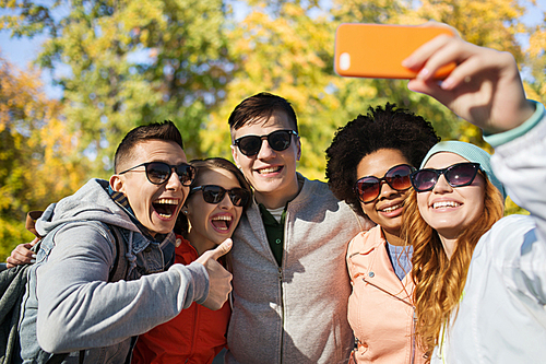 people, season, friendship and technology concept - group of smiling teenage friends taking selfie with smartphone and showing thumbs up over autumn park background