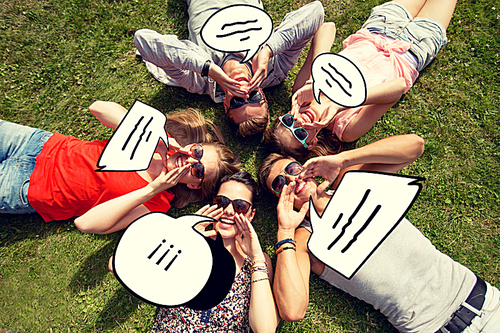 friendship, leisure, summer, message and people concept - group of smiling friends lying with text bubble doodles in circle on grass outdoors