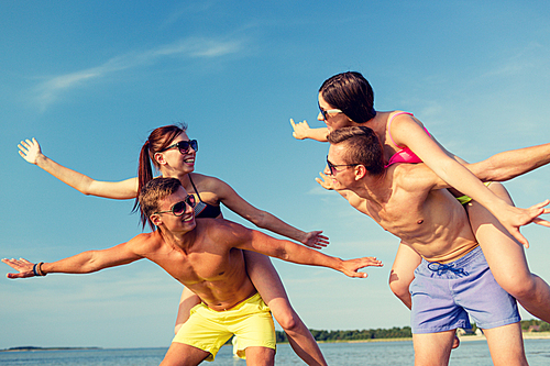 friendship, sea, summer vacation, holidays and people concept - group of smiling friends wearing swimwear and sunglasses having fun on beach