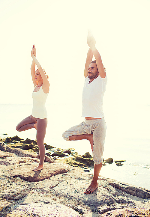 fitness, sport, friendship and lifestyle concept - couple making yoga exercises on beach