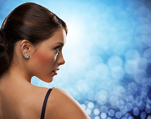 people, jewelry, luxury and glamour concept - woman with diamond earrings over blue lights background