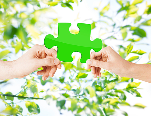 nature, ecology, energy saving, people and environment concept - close up of couple hands with green puzzle over natural background