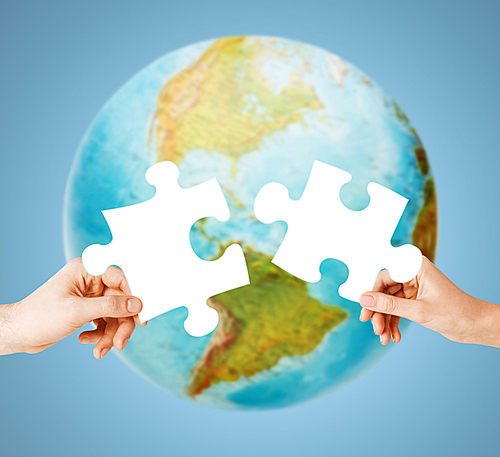 ecology, energy saving, people and environment concept - close up of couple hands trying to connect white puzzle pieces over earth globe on blue background