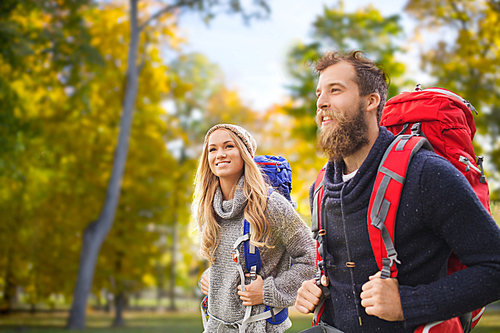 adventure, travel, tourism, hike and people concept - smiling couple walking with backpacks over autumn forest background