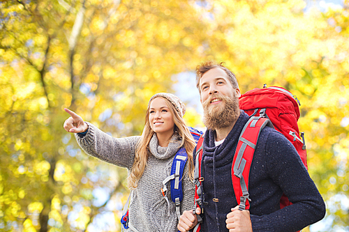 adventure, travel, tourism, hike and people concept - smiling couple walking with backpacks over autumn natural background